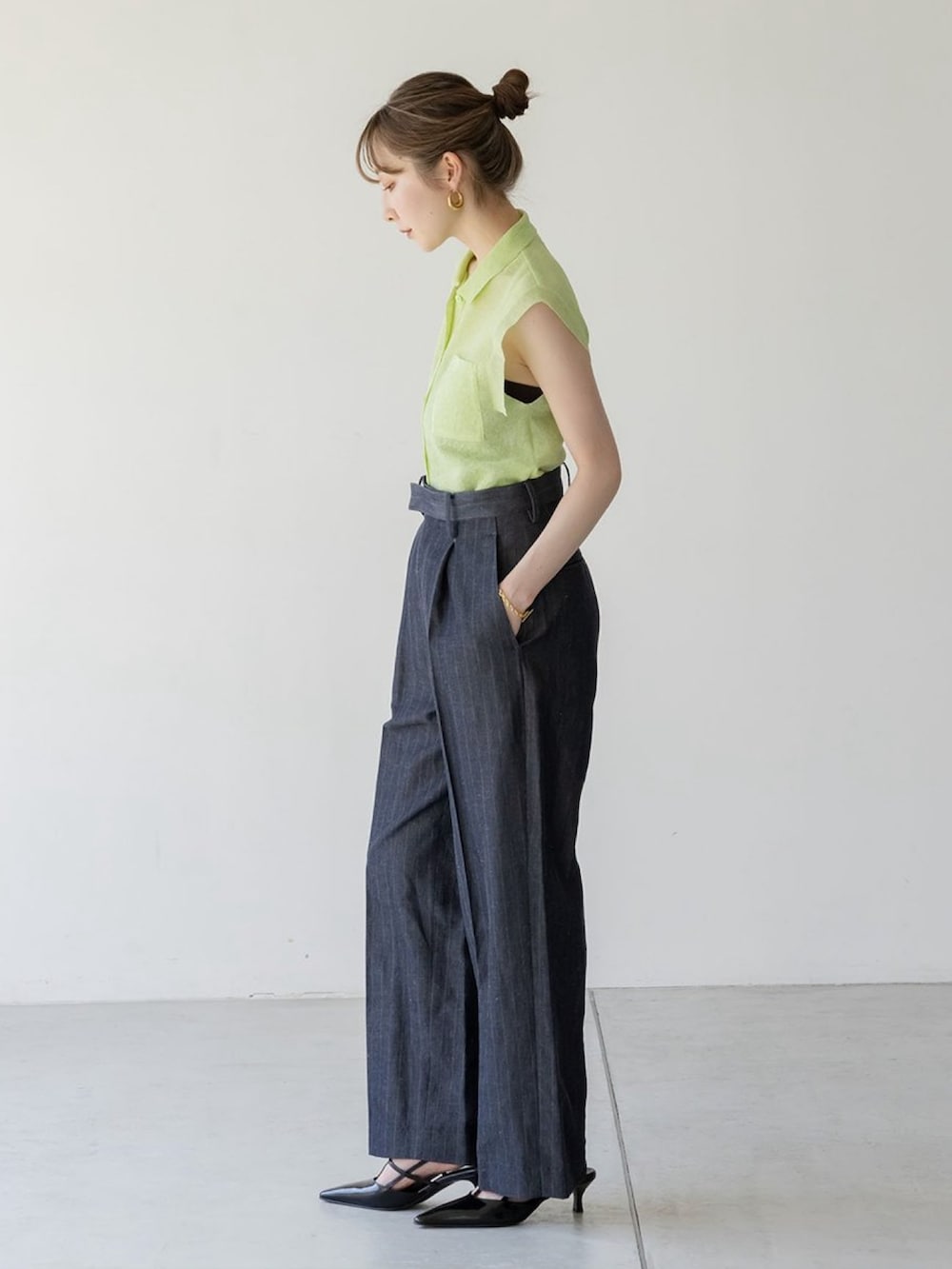 グリーン系のニット/セーター、ブルー系のスラックス、ホワイト系のショルダーバッグを着用したレディースの夏コーディネートの2枚目の写真