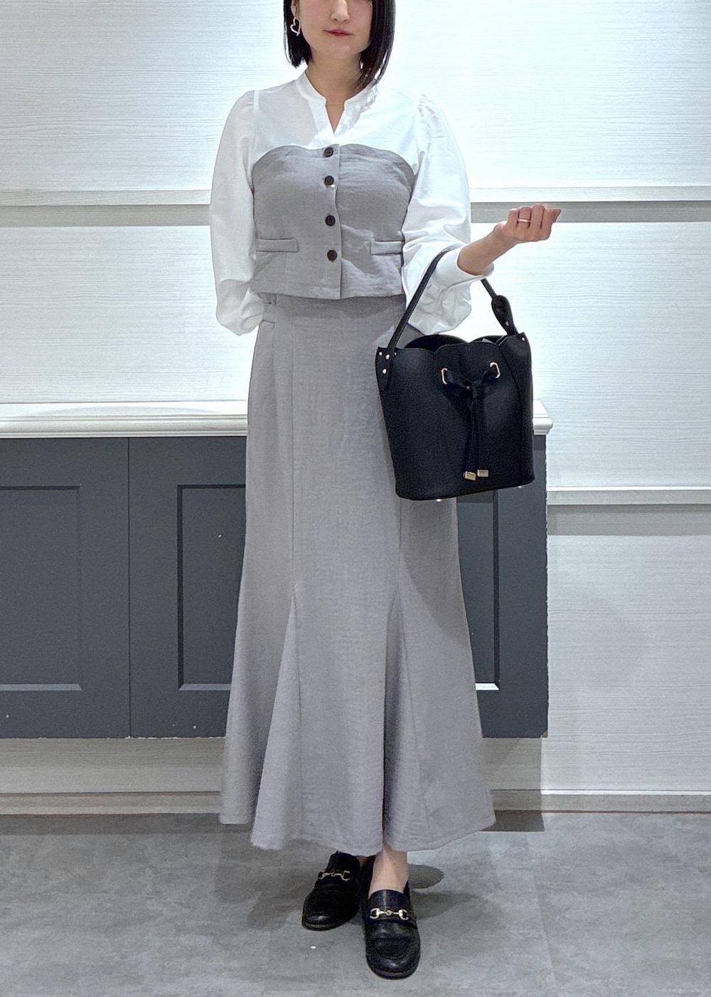 ブラック系のショルダーバッグ、ブラック系のローファー、グレー系のスカートを着用したレディースの春コーディネートの2枚目の写真