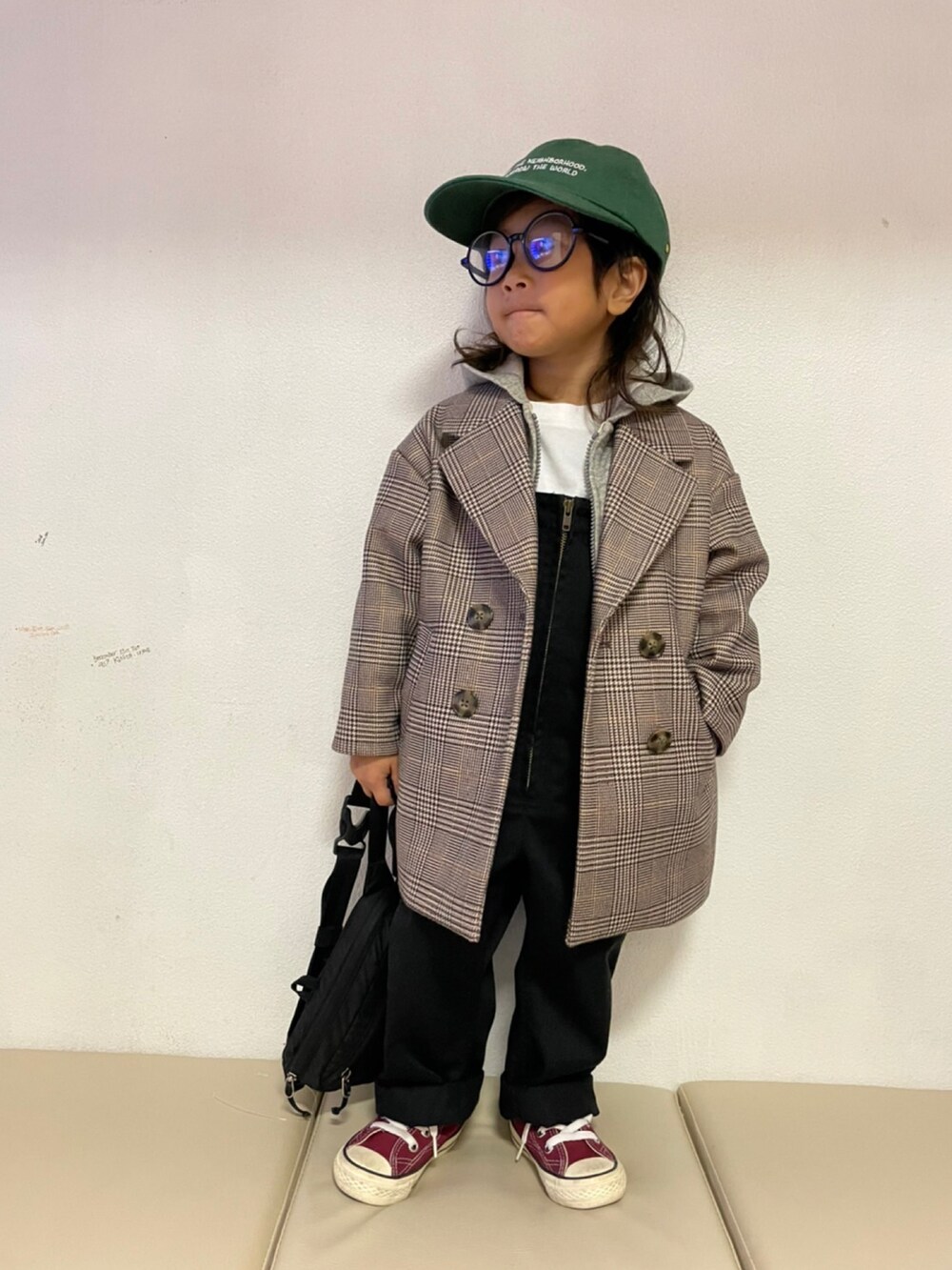 ベージュ系のチェスターコート、グレー系のパーカー、ブラック系のサロペット/オーバーオールを着用したキッズの冬コーディネートの2枚目の写真