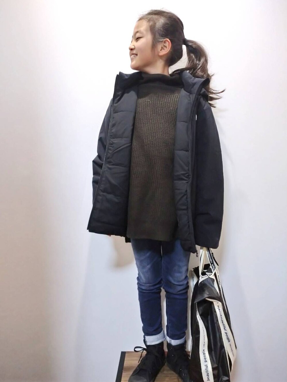 ブラック系のダウンジャケット/コート、ブラウン系のニット/セーター、ブルー系のデニムパンツを着用したキッズの冬コーディネートの2枚目の写真