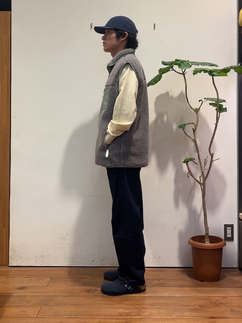 グレー系のベスト、ホワイト系のニット/セーター、ブルー系のデニムパンツを着用したメンズの秋コーディネートの2枚目の写真