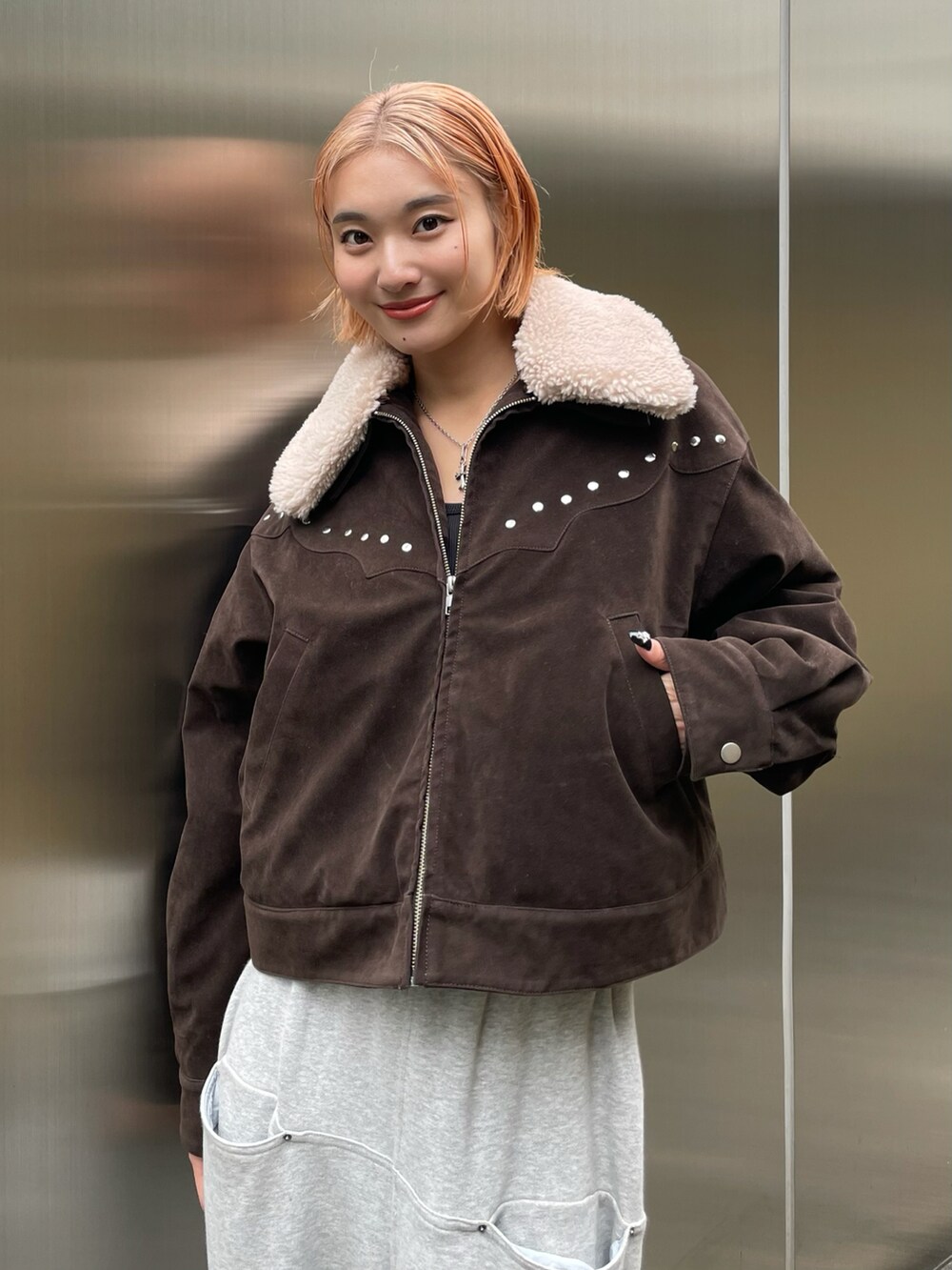 ブラウン系のブルゾン、グレー系のスウェットパンツ、シルバー系のネックレスを着用したレディースの秋コーディネートの2枚目の写真