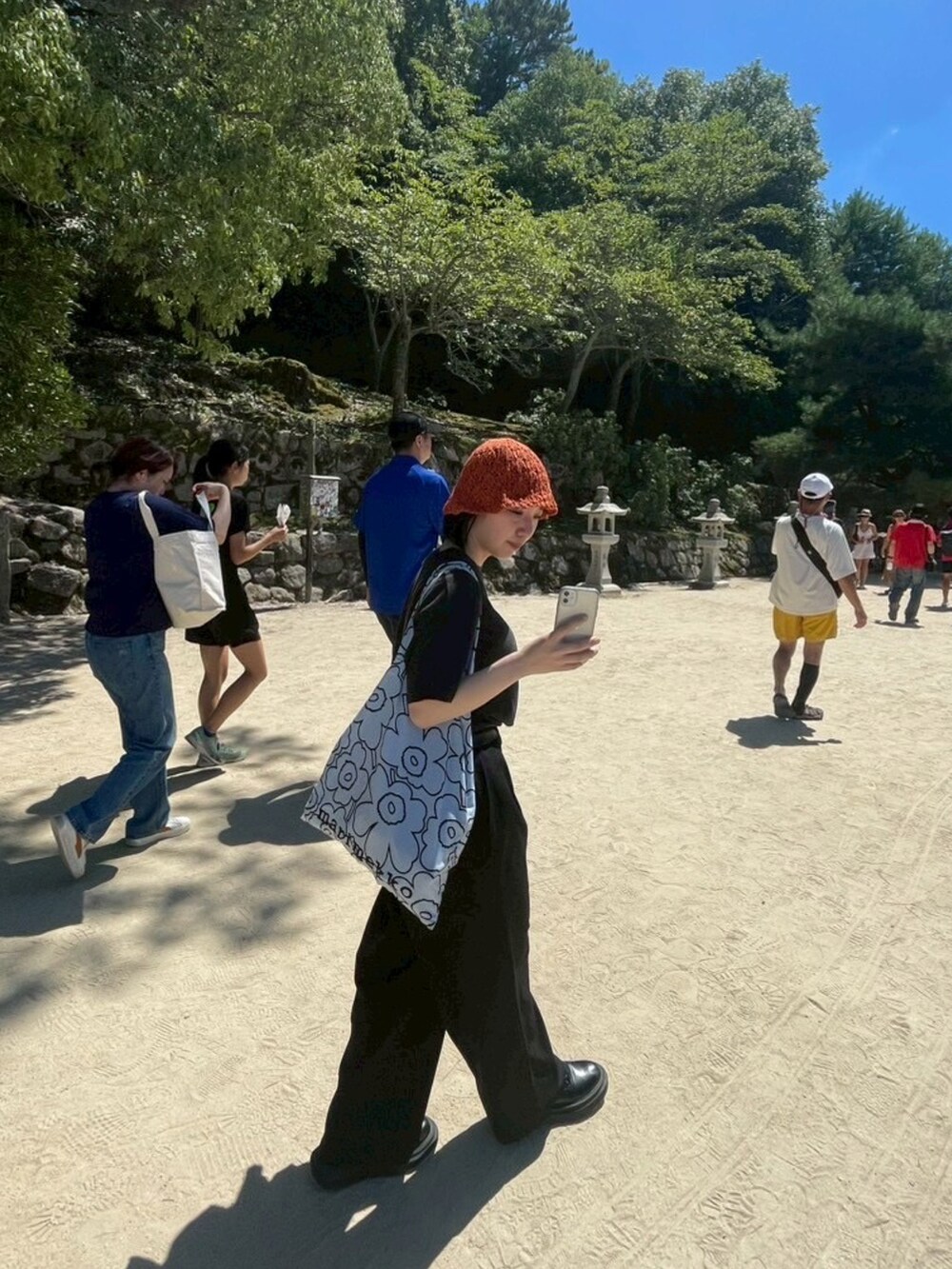 ブルー系のトートバッグ、ブラック系のパンツ、オレンジ系のハットを着用したレディースの夏コーディネートの2枚目の写真