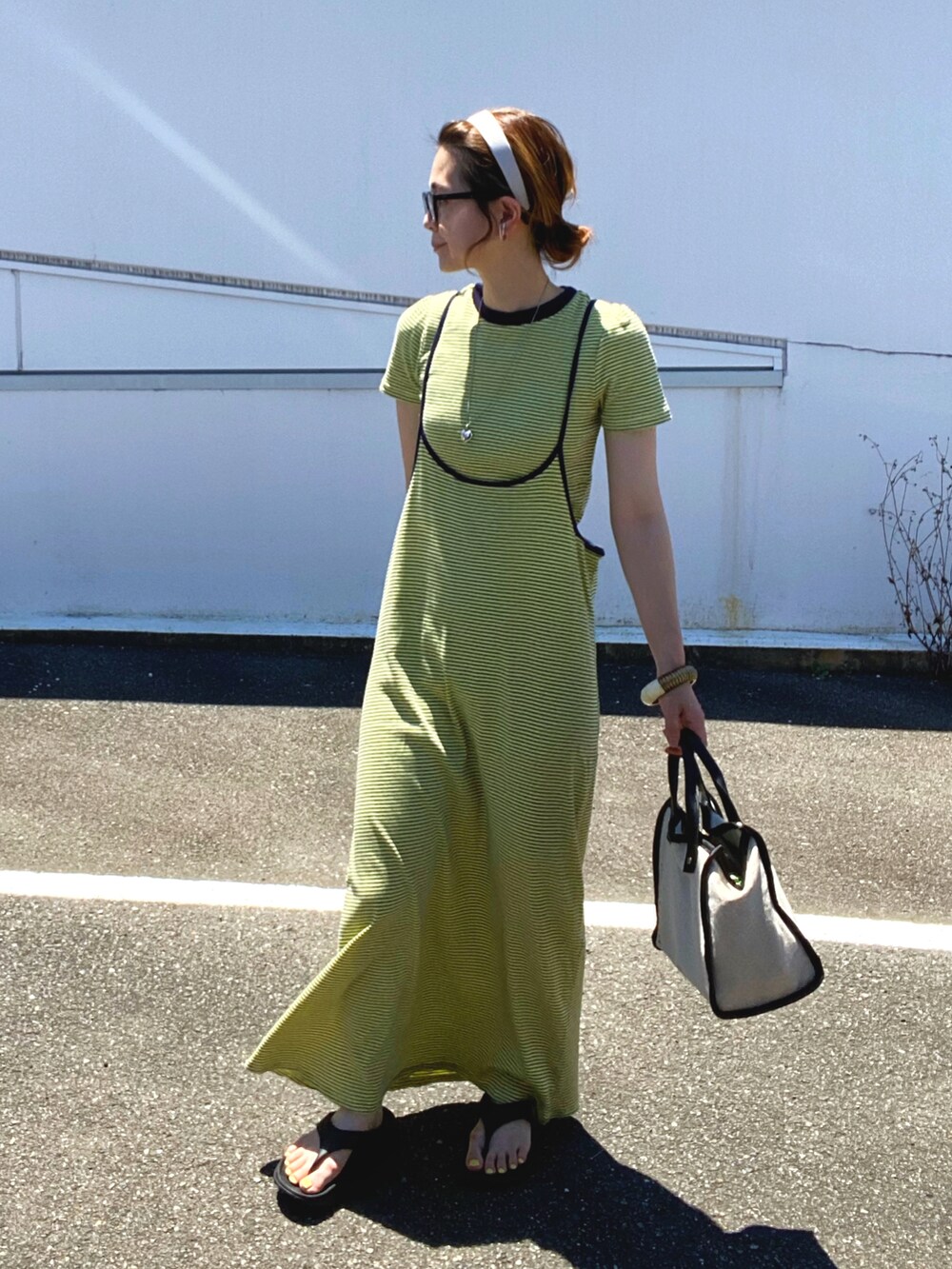 イエロー系のワンピース、ベージュ系のトートバッグ、シルバー系のネックレスを着用したレディースの夏コーディネートの2枚目の写真