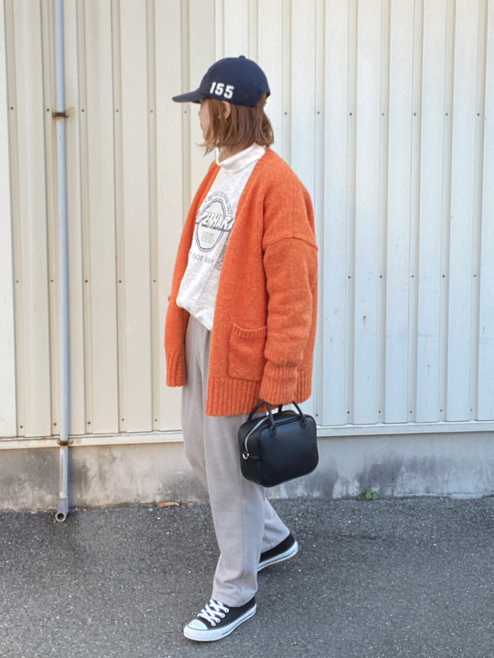 オレンジ系のカーディガン/ボレロ、ブラック系のボストンバッグ、グレー系のスラックスを着用したレディースの冬コーディネートの2枚目の写真