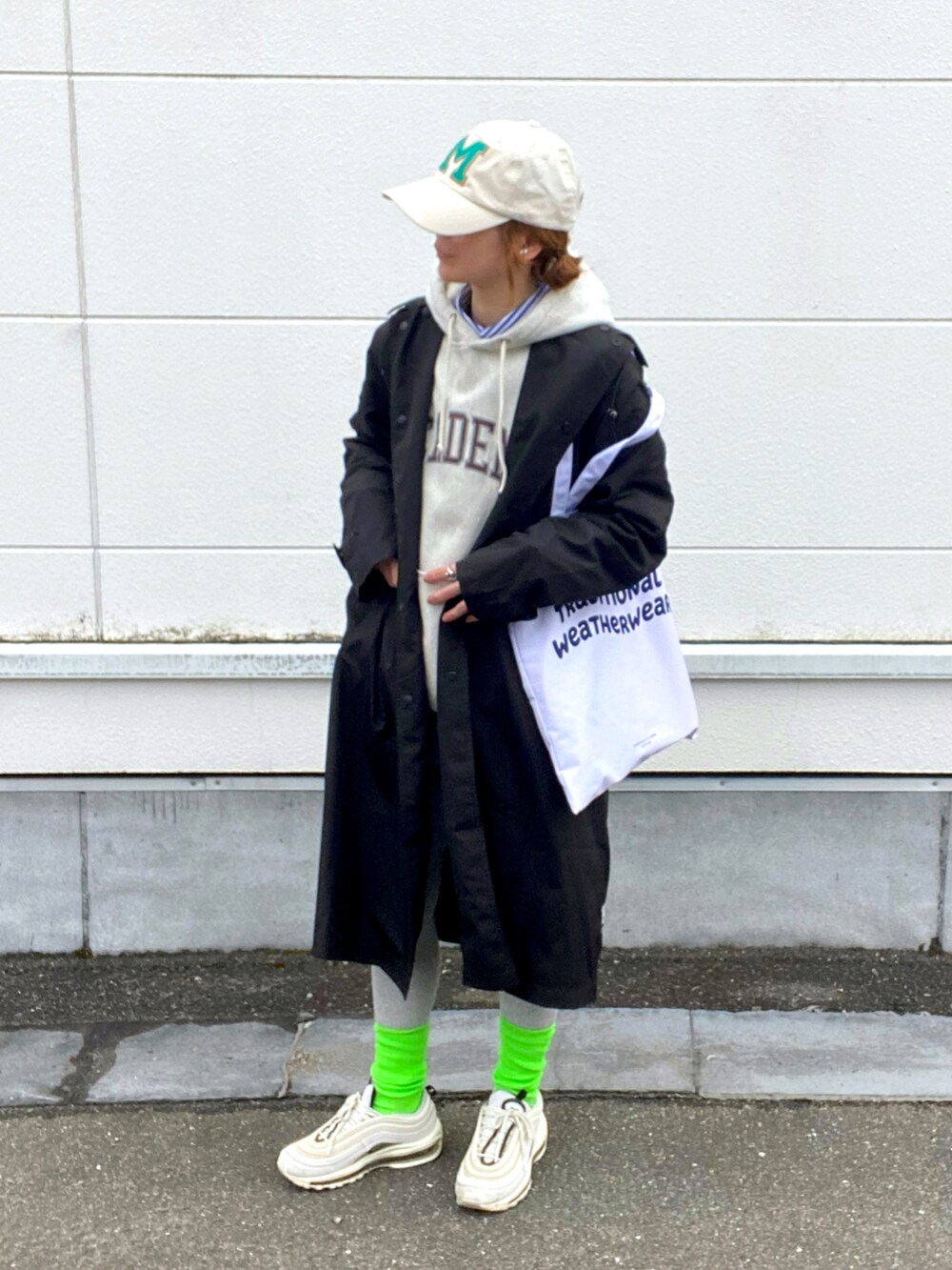 ホワイト系のトートバッグ、ホワイト系のスニーカー、ブラック系のレインコート/ポンチョを着用したレディースの春コーディネートの2枚目の写真