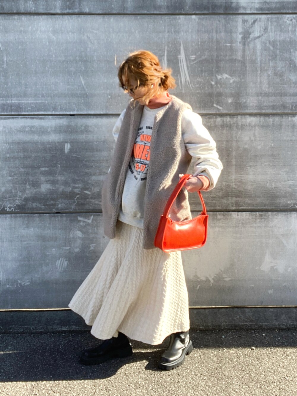 ベージュ系のベスト、ホワイト系のスカート、オレンジ系のショルダーバッグを着用したレディースの冬コーディネートの3枚目の写真