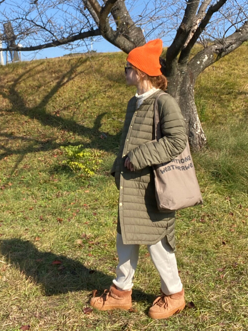 グリーン系のダウンジャケット/コート、ホワイト系のニット/セーター、ブラウン系のトートバッグを着用したレディースの冬コーディネートの2枚目の写真