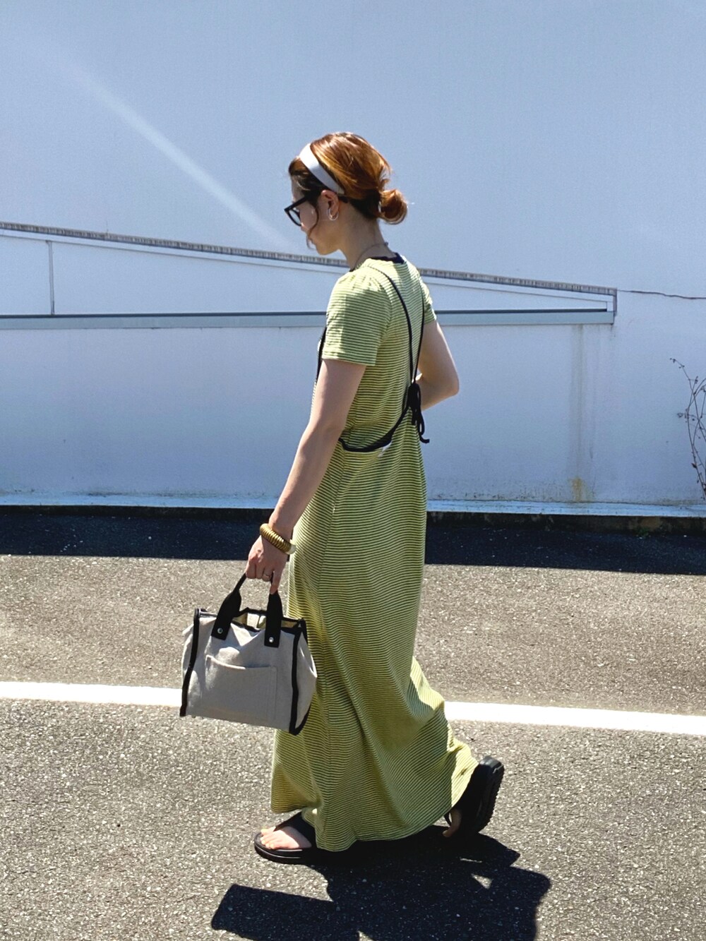 イエロー系のワンピース、ベージュ系のトートバッグ、シルバー系のネックレスを着用したレディースの夏コーディネートの3枚目の写真