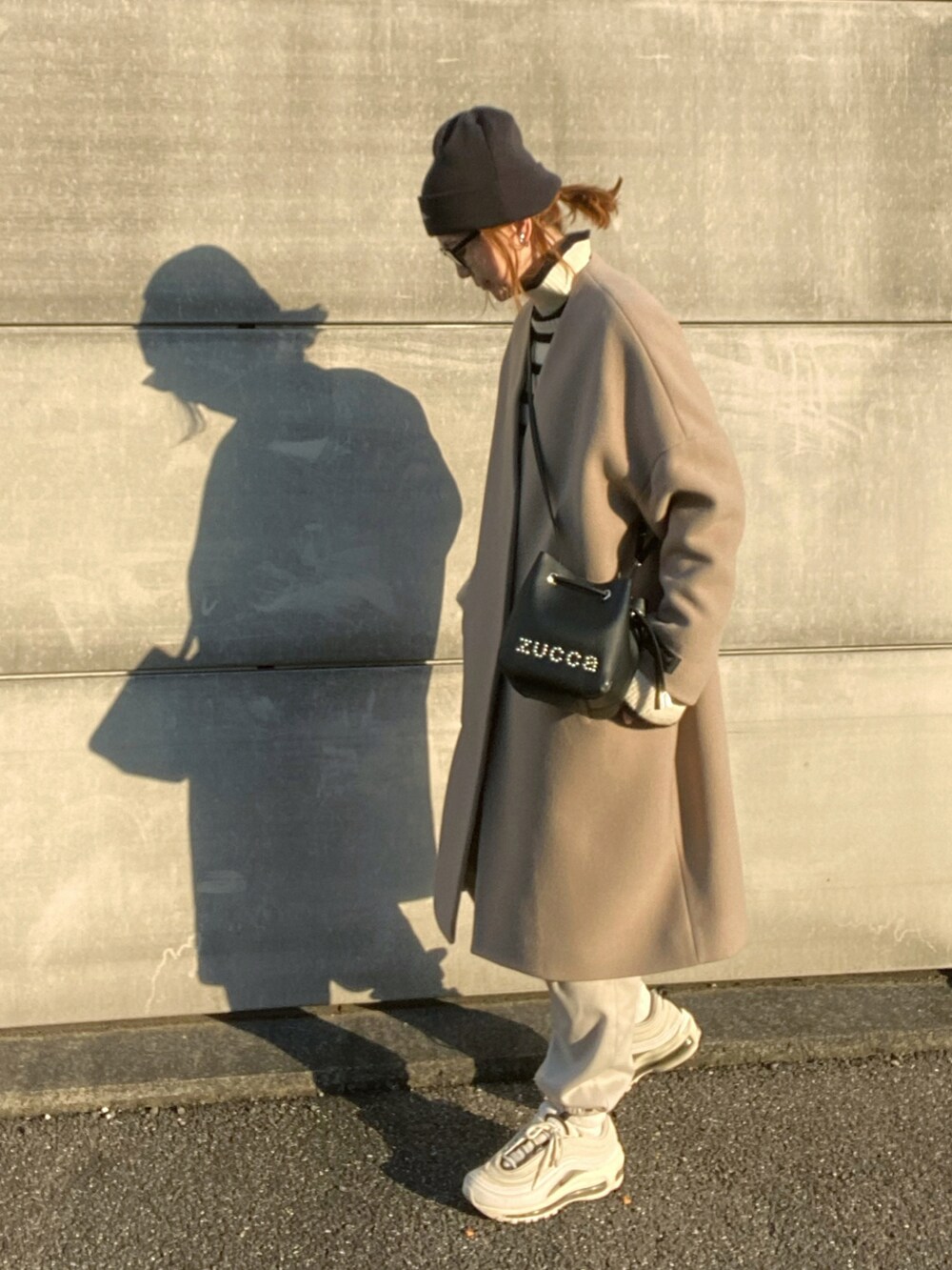 ブラック系のショルダーバッグ、ブラウン系のその他アウター、ホワイト系のニット/セーターを着用したレディースの冬コーディネートの2枚目の写真