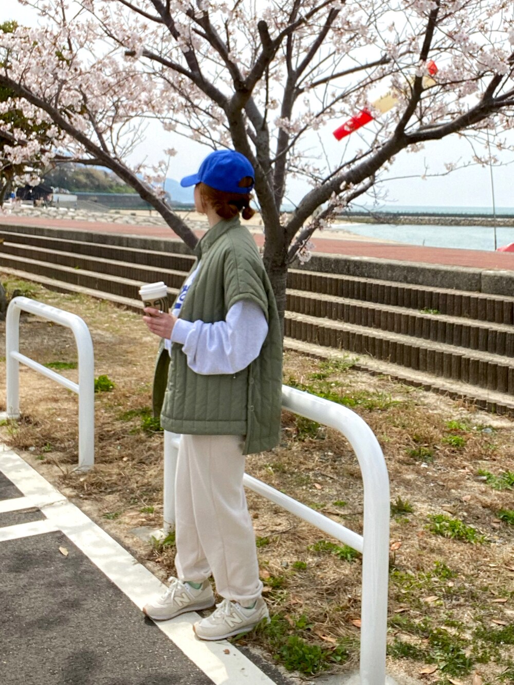 グリーン系のベスト、ホワイト系のスニーカー、ブルー系のキャップを着用したレディースの春コーディネートの3枚目の写真