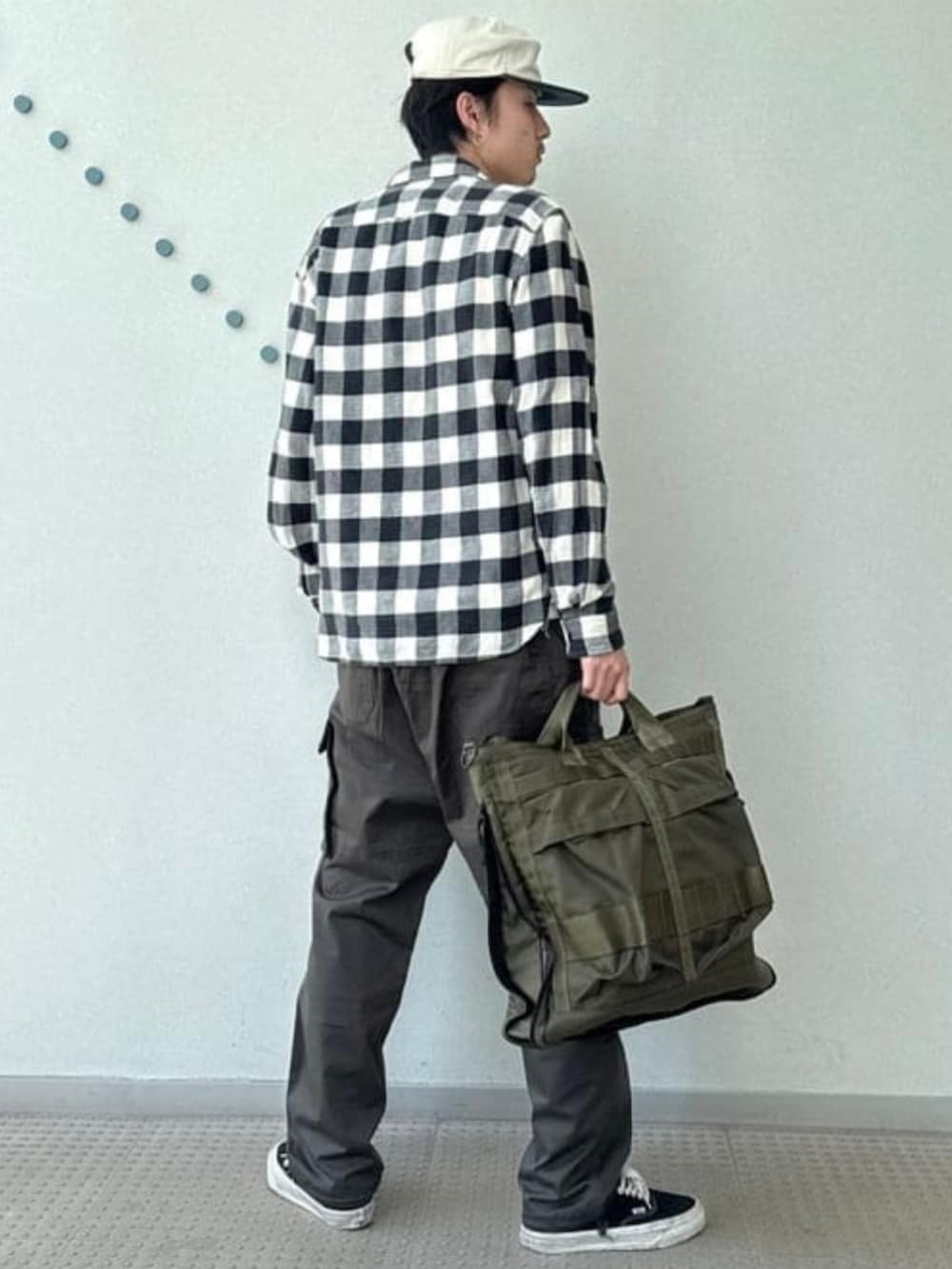 グリーン系のトートバッグ、ブラック系のスニーカー、グレー系のカーゴパンツを着用したメンズの夏コーディネートの2枚目の写真