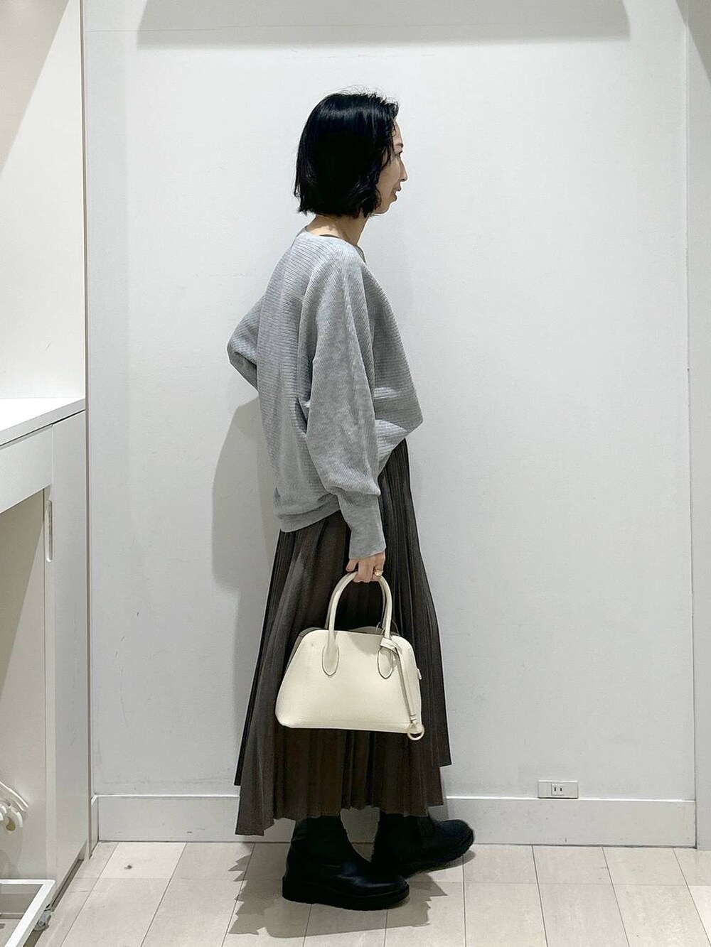 ホワイト系のショルダーバッグ、ブラック系のブーツ、グレー系のスカートを着用したレディースの冬コーディネートの2枚目の写真