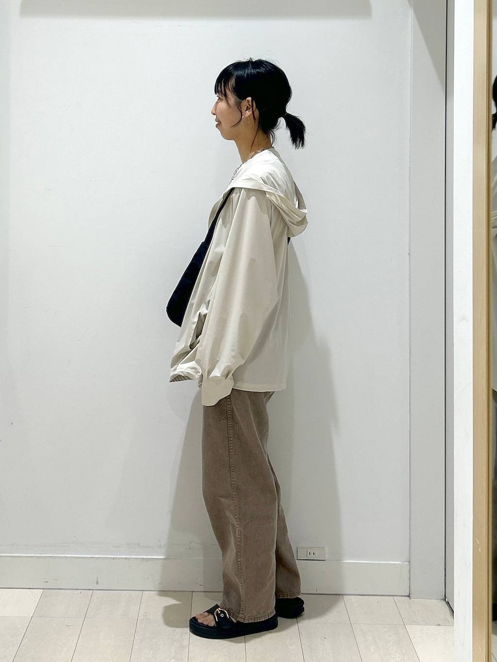 ブラック系のショルダーバッグ、ブラウン系のデニムパンツ、ベージュ系のマウンテンパーカーを着用したレディースの夏コーディネートの4枚目の写真