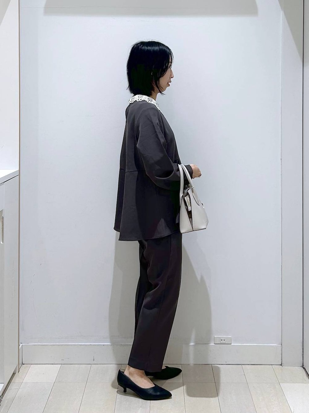 ホワイト系のショルダーバッグ、グレー系のセットアップ、ブラック系のパンプスを着用したレディースの冬コーディネートの2枚目の写真