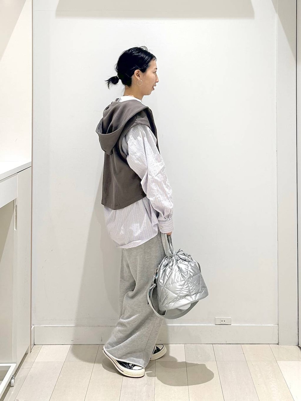 シルバー系のハンドバッグ、グレー系のスウェットパンツ、ブラウン系のベストを着用したレディースの春コーディネートの2枚目の写真