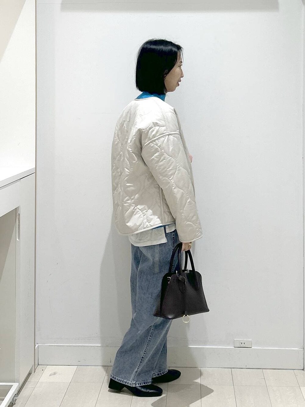 ブラウン系のショルダーバッグ、ベージュ系のブルゾン、ブルー系のデニムパンツを着用したレディースの冬コーディネートの2枚目の写真