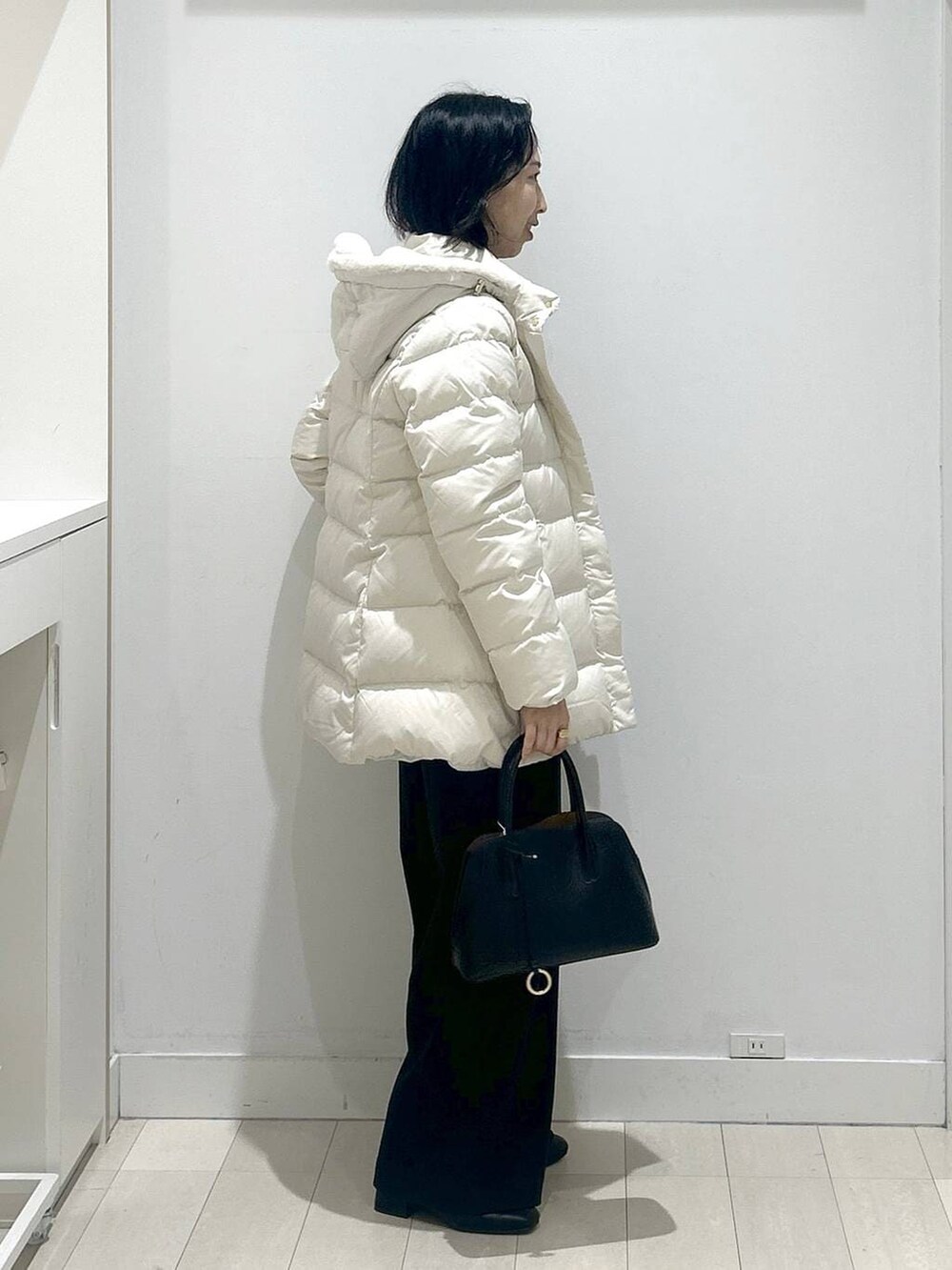 ブラック系のショルダーバッグ、ベージュ系のダウンジャケット/コート、ホワイト系のTシャツ/カットソーを着用したレディースの冬コーディネートの2枚目の写真