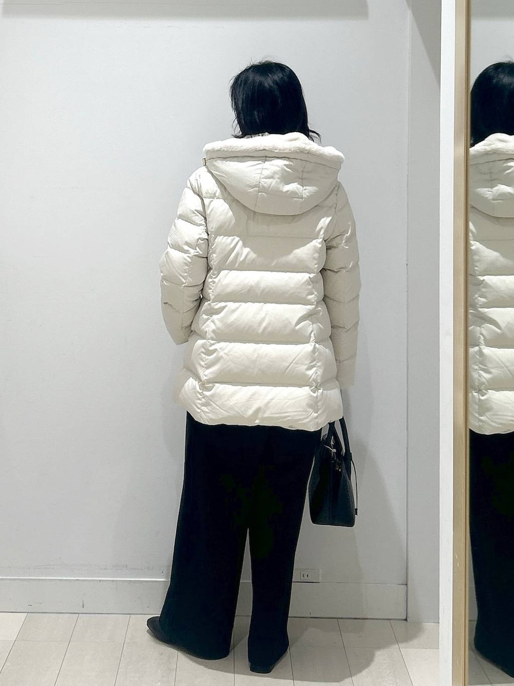 ブラック系のショルダーバッグ、ベージュ系のダウンジャケット/コート、ホワイト系のTシャツ/カットソーを着用したレディースの冬コーディネートの3枚目の写真