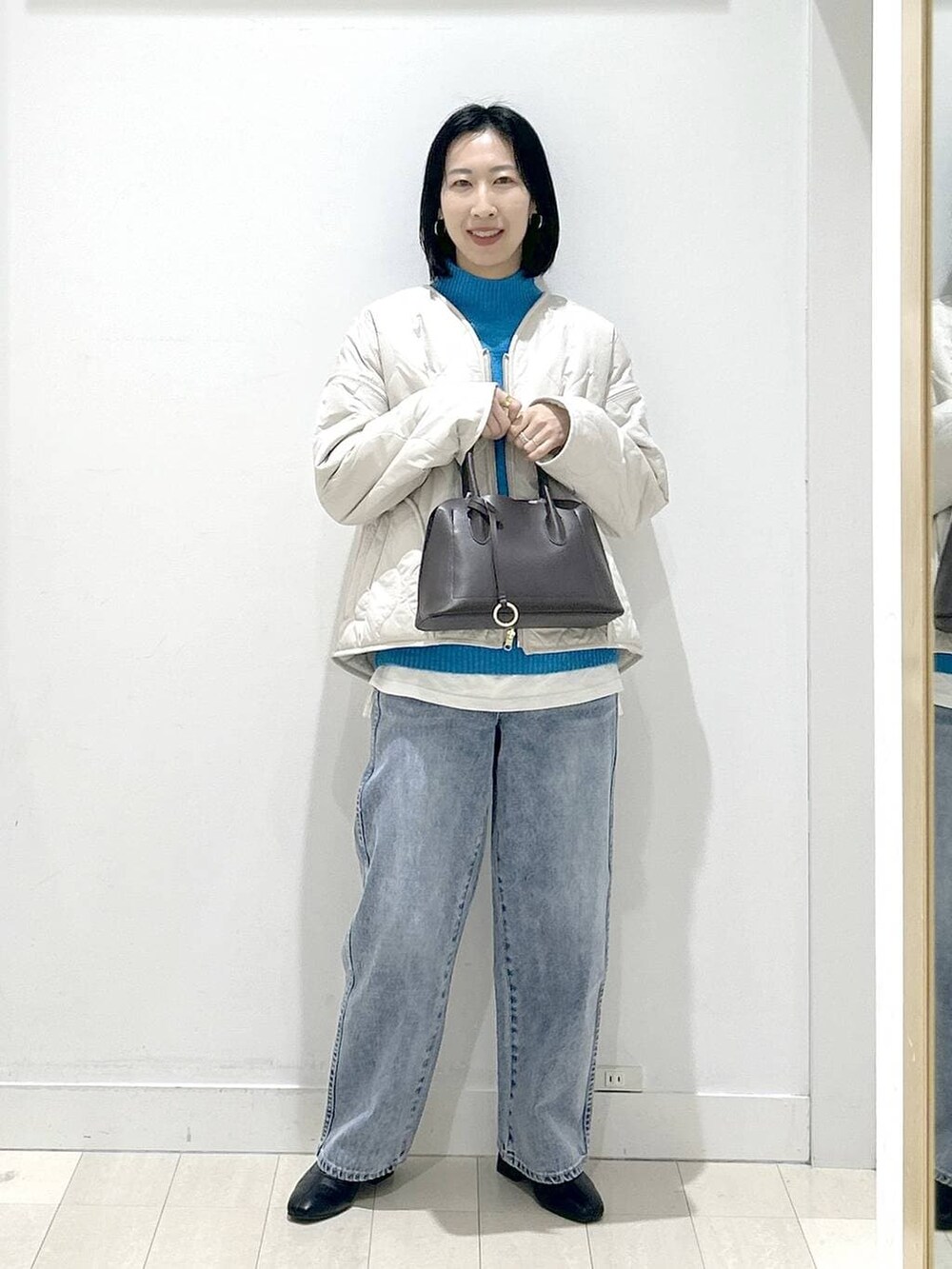 ブラウン系のショルダーバッグ、ベージュ系のブルゾン、ブルー系のデニムパンツを着用したレディースの冬コーディネートの5枚目の写真