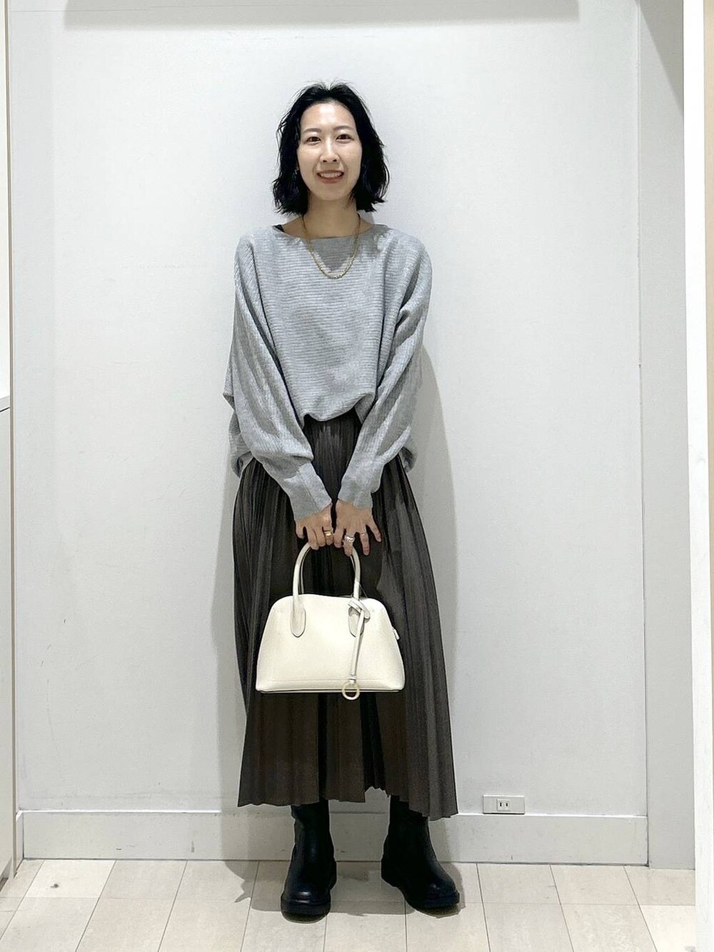 ホワイト系のショルダーバッグ、ブラック系のブーツ、グレー系のスカートを着用したレディースの冬コーディネートの5枚目の写真