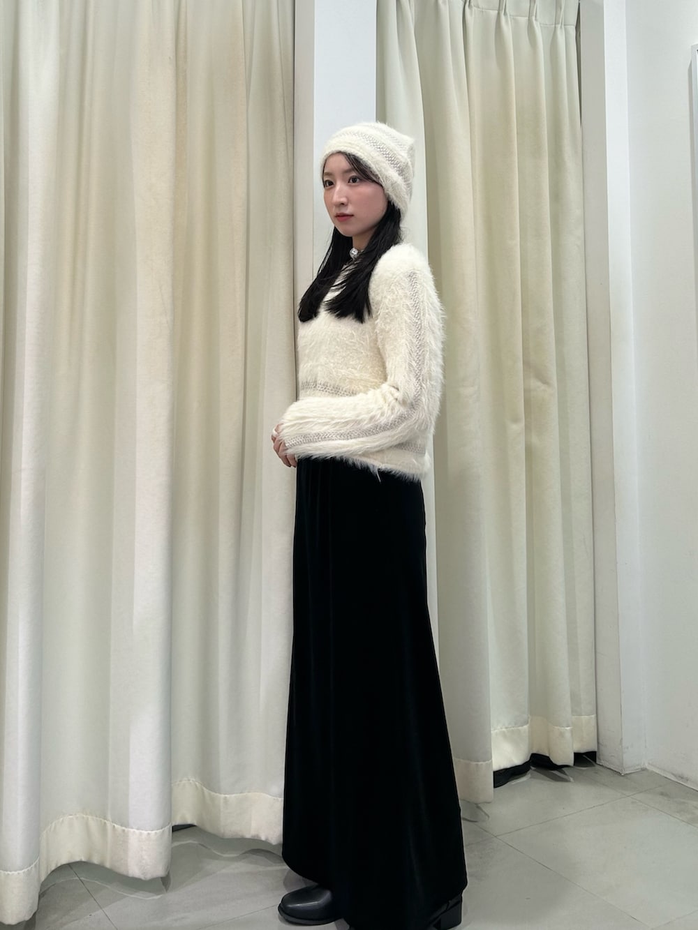 ホワイト系のニット/セーター、ブラック系のスカート、ブラック系のブーツを着用したレディースの秋コーディネートの2枚目の写真