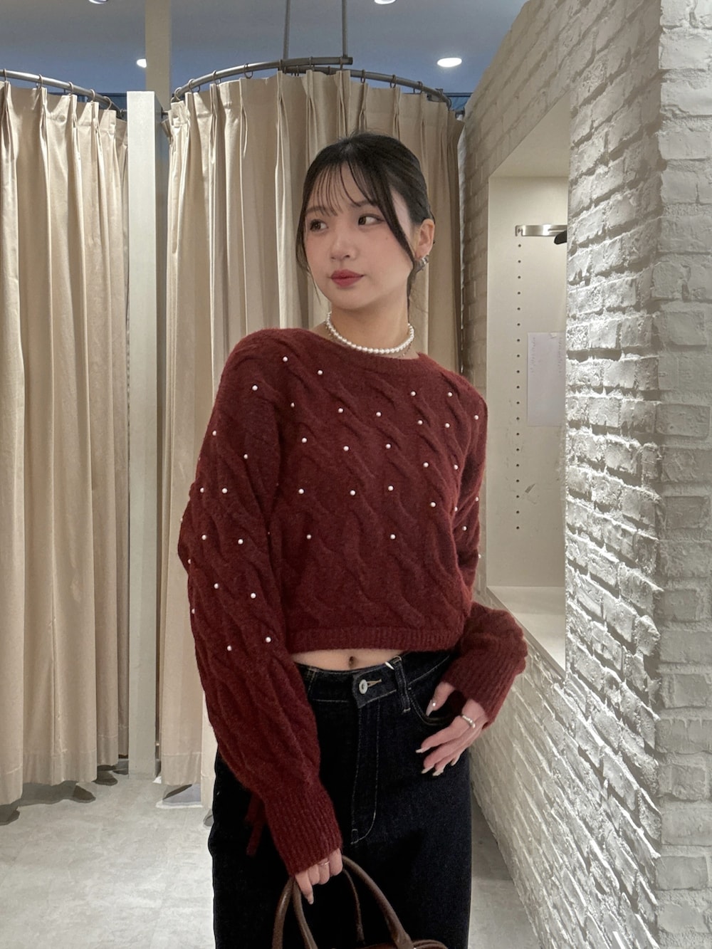 レッド系のニット/セーター、ブルー系のデニムパンツ、ブラウン系のハンドバッグを着用したレディースの冬コーディネートの3枚目の写真