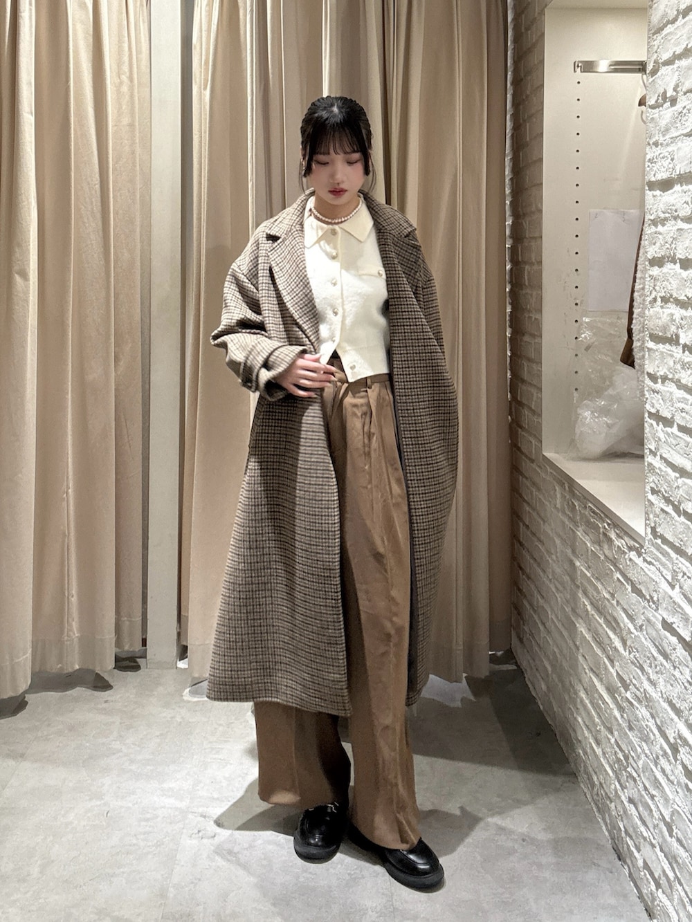 ホワイト系のニット/セーター、ブラウン系のスラックス、ベージュ系のチェスターコートを着用したレディースの冬コーディネートの2枚目の写真