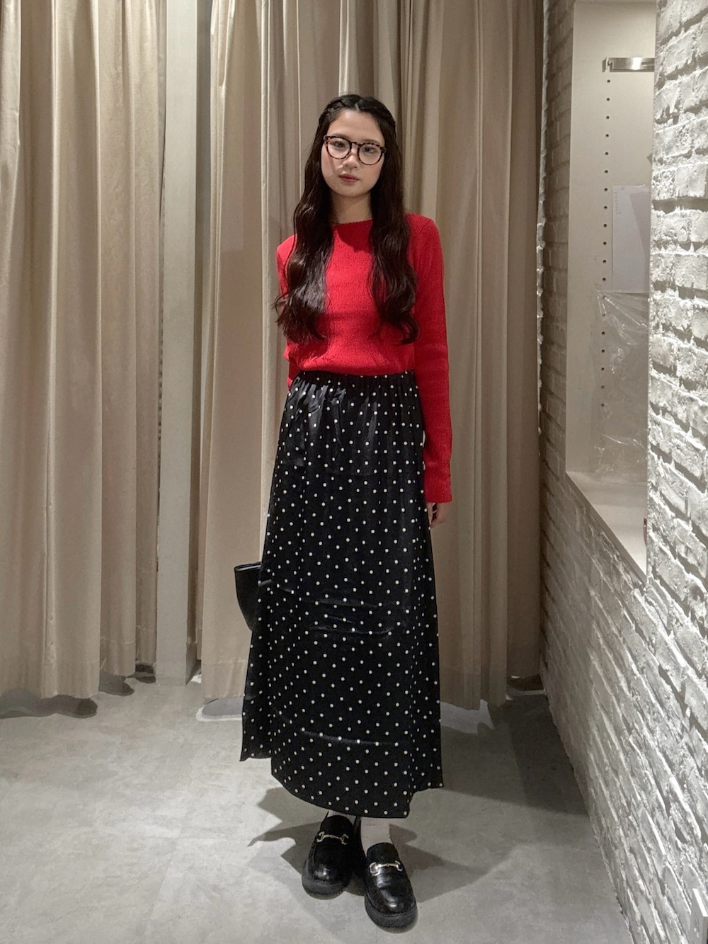 レッド系のニット/セーター、ブラック系のスカート、ブラウン系のサングラスを着用したレディースの秋コーディネートの2枚目の写真