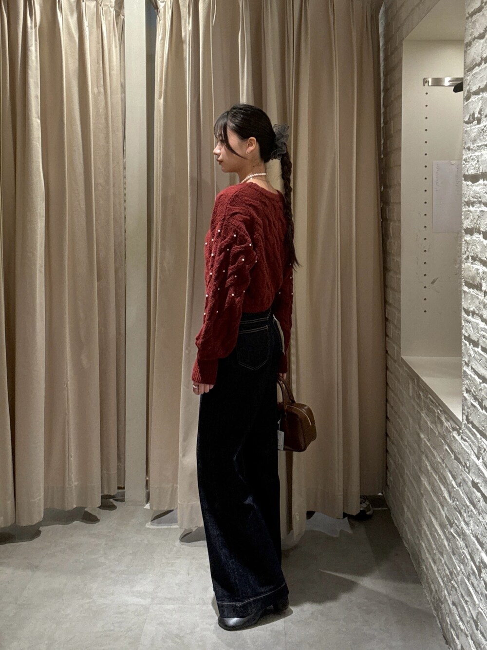 レッド系のニット/セーター、ブルー系のデニムパンツ、ブラウン系のハンドバッグを着用したレディースの冬コーディネートの2枚目の写真