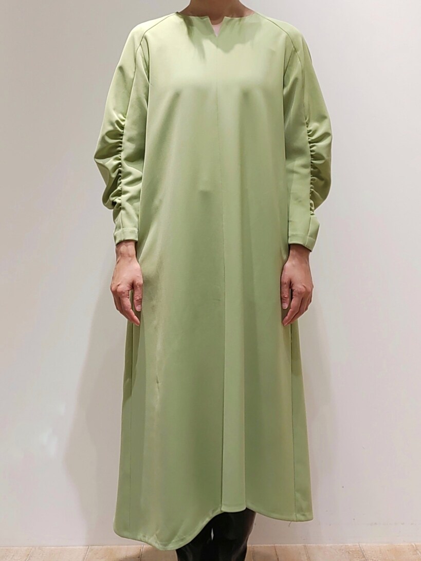 ブラック系のノーカラーコート、グリーン系のワンピースを着用したレディースの冬コーディネートの2枚目の写真