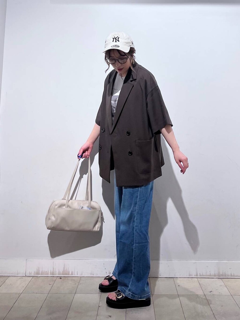 ブルー系のデニムパンツ、ホワイト系のTシャツ/カットソー、ベージュ系のショルダーバッグを着用したレディースの春コーディネートの3枚目の写真