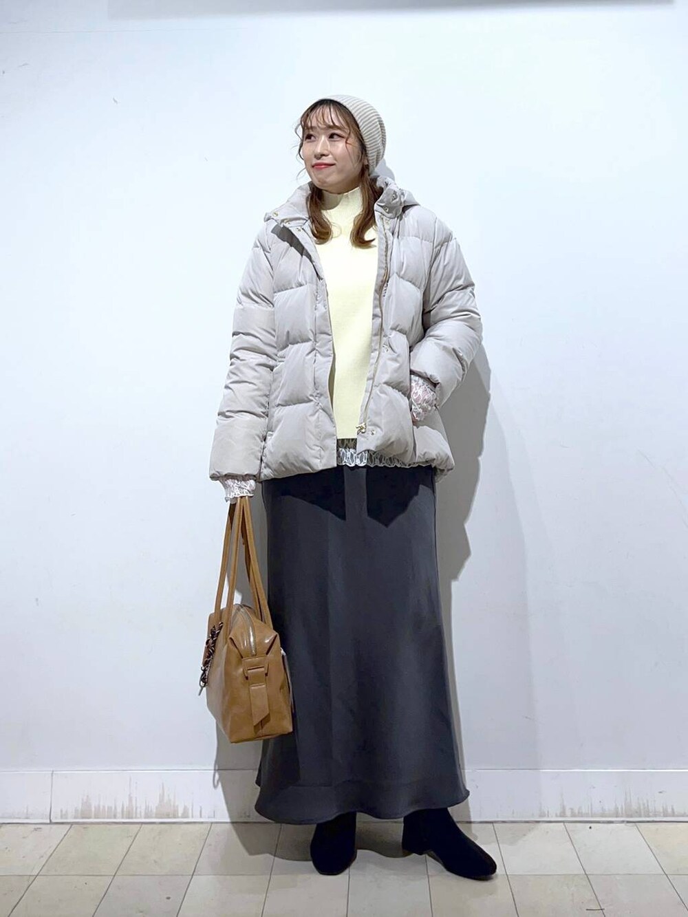 ブラウン系のボストンバッグ、ベージュ系のダウンジャケット/コート、ホワイト系のTシャツ/カットソーを着用したレディースの冬コーディネートの2枚目の写真