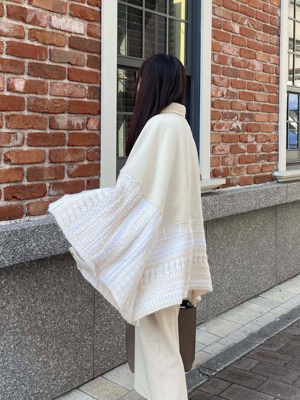 ホワイト系のポンチョ、ホワイト系のスカート、ベージュ系のブーツを着用したレディースの冬コーディネートの5枚目の写真