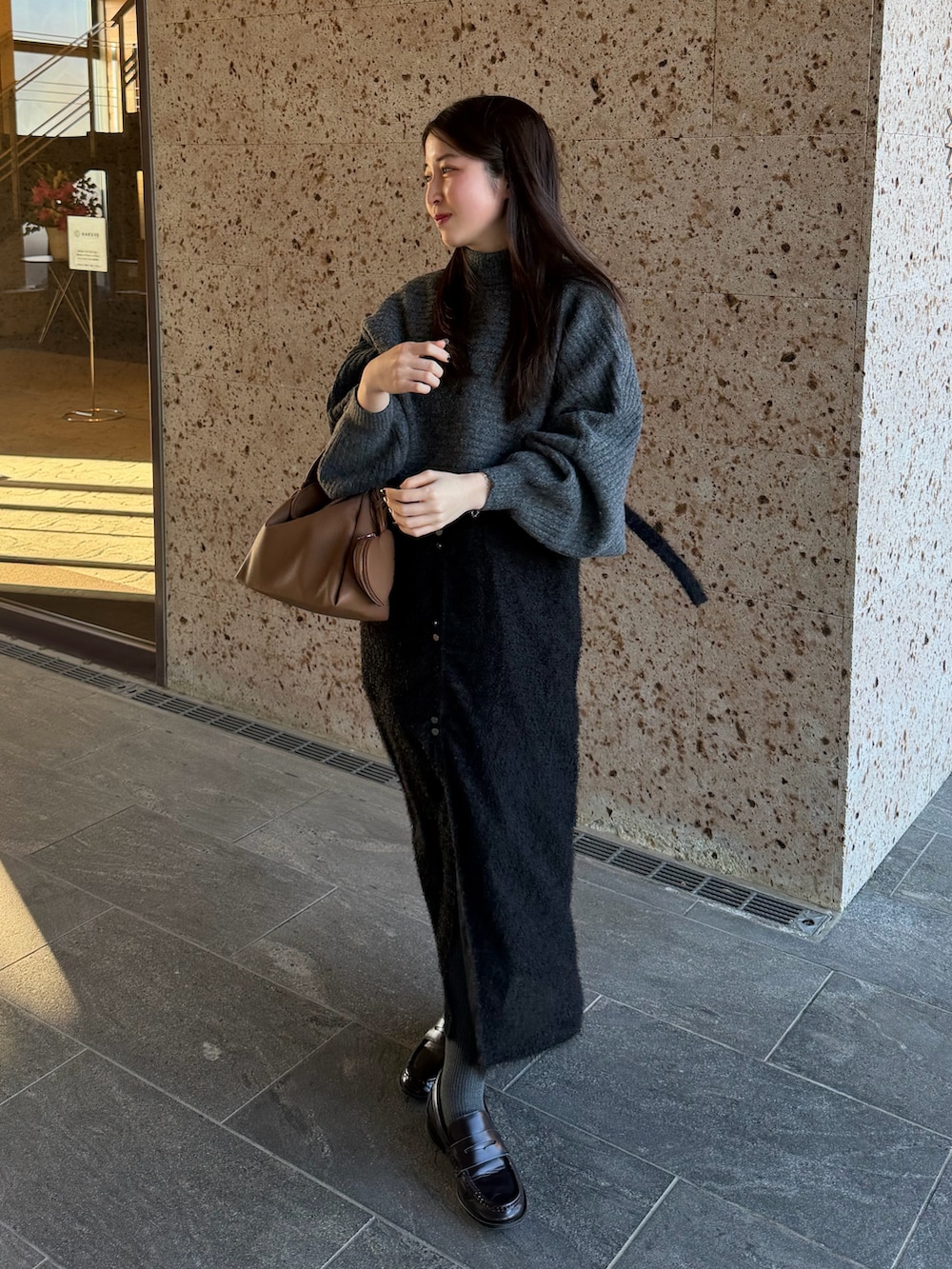 グレー系のワンピース、ブラウン系のスカート、イエロー系のハンドバッグを着用したレディースの冬コーディネートの2枚目の写真