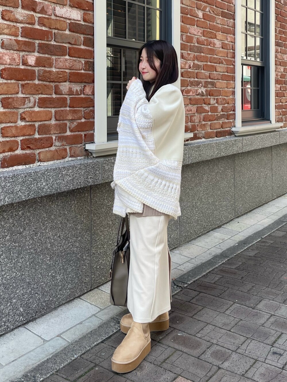 ホワイト系のポンチョ、ホワイト系のスカート、ベージュ系のブーツを着用したレディースの冬コーディネートの4枚目の写真
