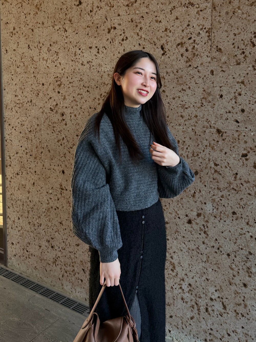 グレー系のワンピース、ブラウン系のスカート、イエロー系のハンドバッグを着用したレディースの冬コーディネートの4枚目の写真