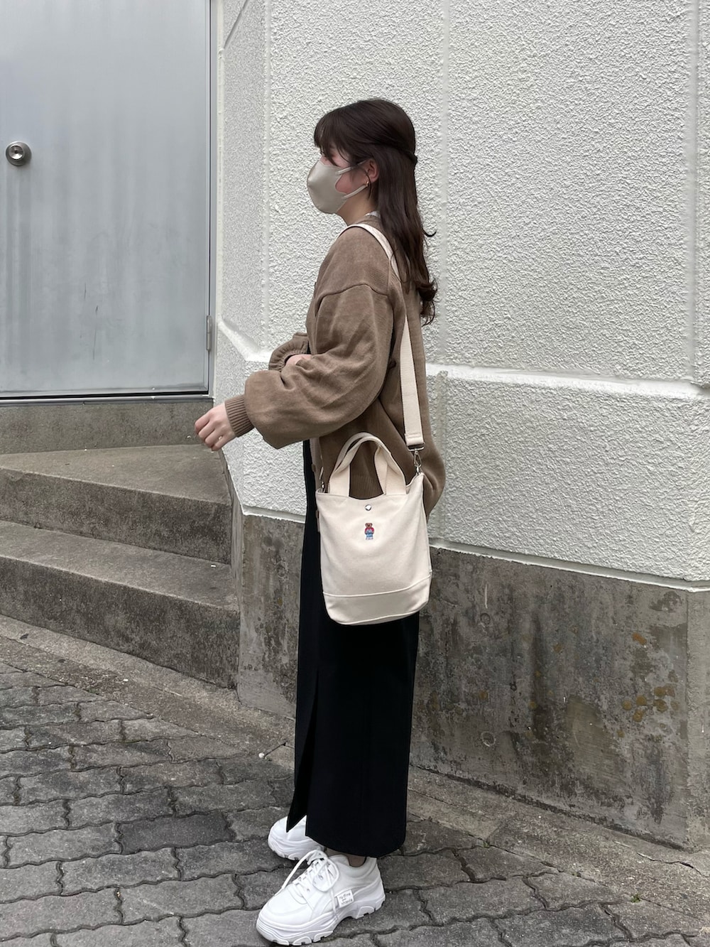 ブラウン系のカーディガン/ボレロ、ブラック系のジャンパースカート、ホワイト系のスニーカーを着用したレディースの冬コーディネートの2枚目の写真
