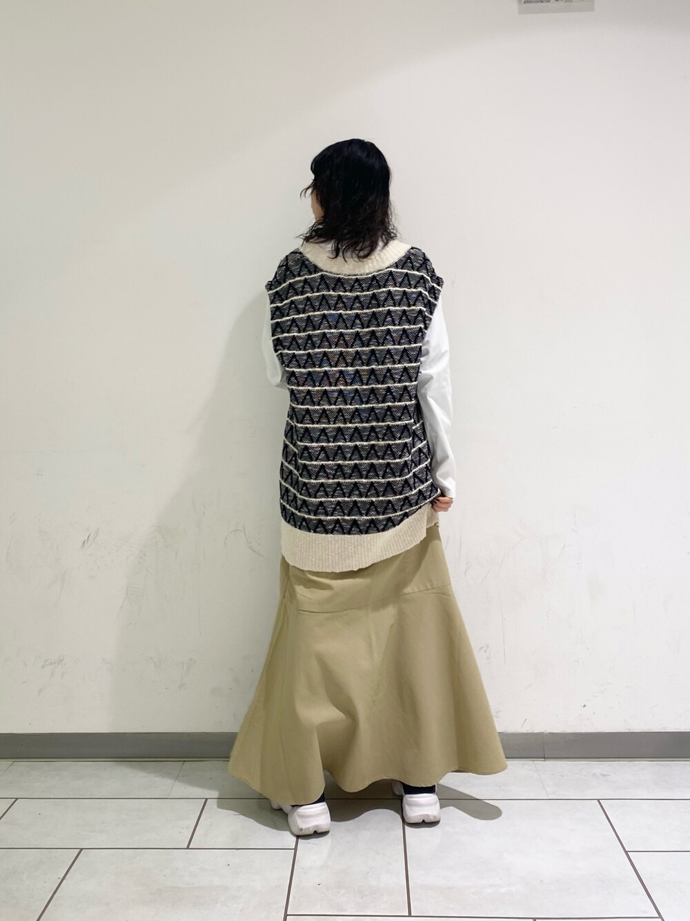 ブラック系のベスト、ベージュ系のスカートを着用したレディースの春コーディネートの2枚目の写真