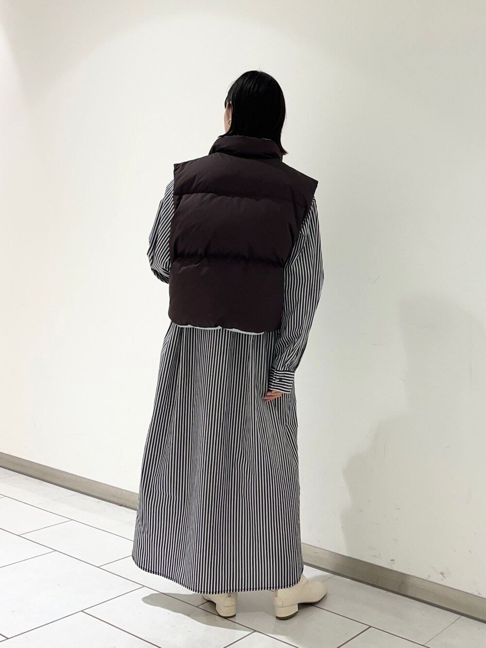 ブラウン系のダウンベスト、ホワイト系のワンピース/ドレス、ホワイト系のブーツを着用したレディースの秋コーディネートの2枚目の写真