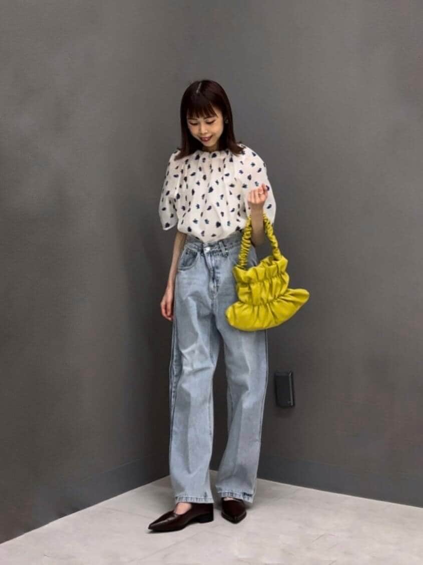 イエロー系のハンドバッグ、ホワイト系のシャツ/ブラウス、ブルー系のデニムパンツを着用したレディースの夏コーディネートの2枚目の写真