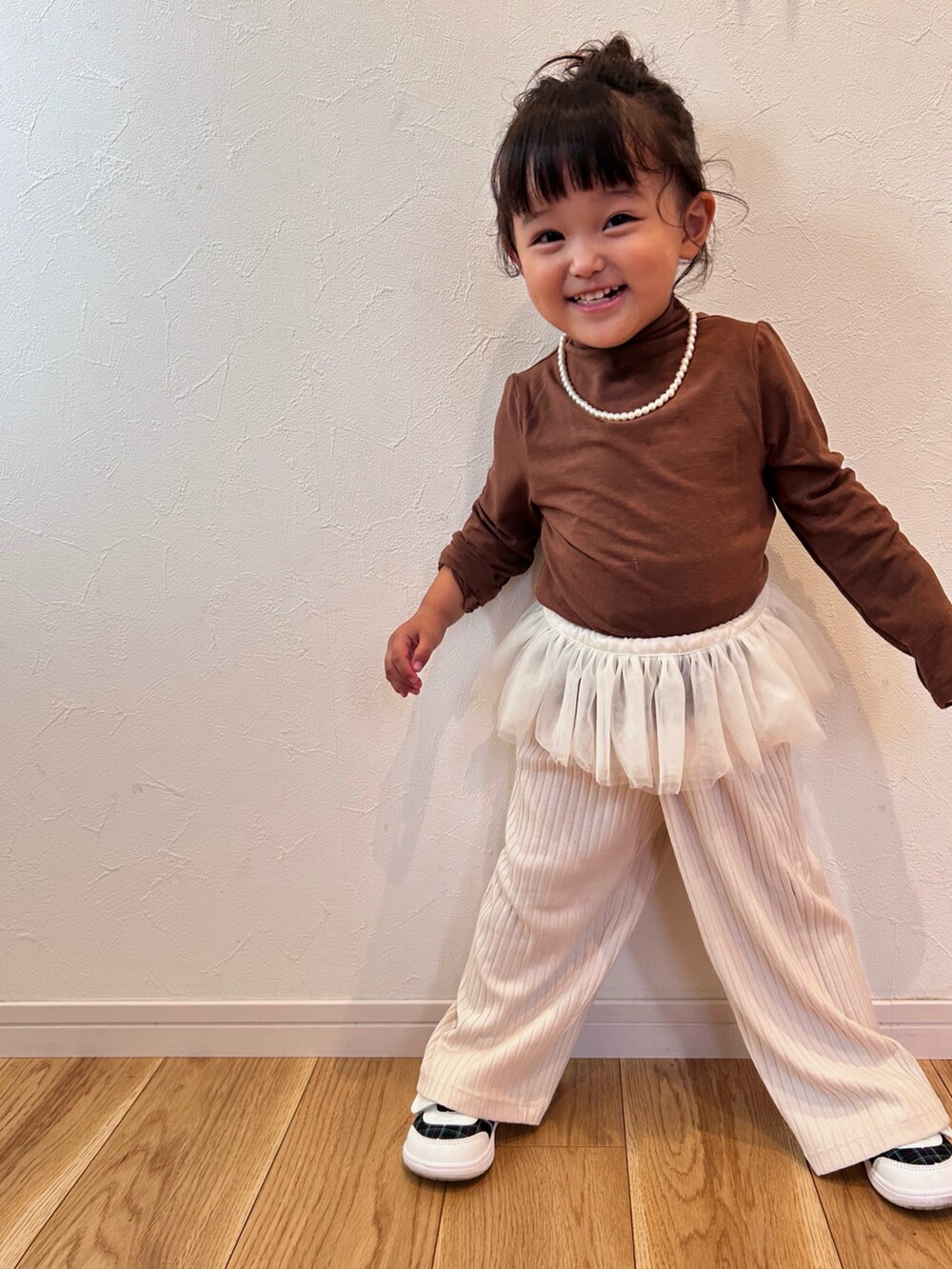 ブラウン系のアンサンブル、ホワイト系のスニーカー、ホワイト系のパンツを着用したキッズの秋コーディネートの2枚目の写真