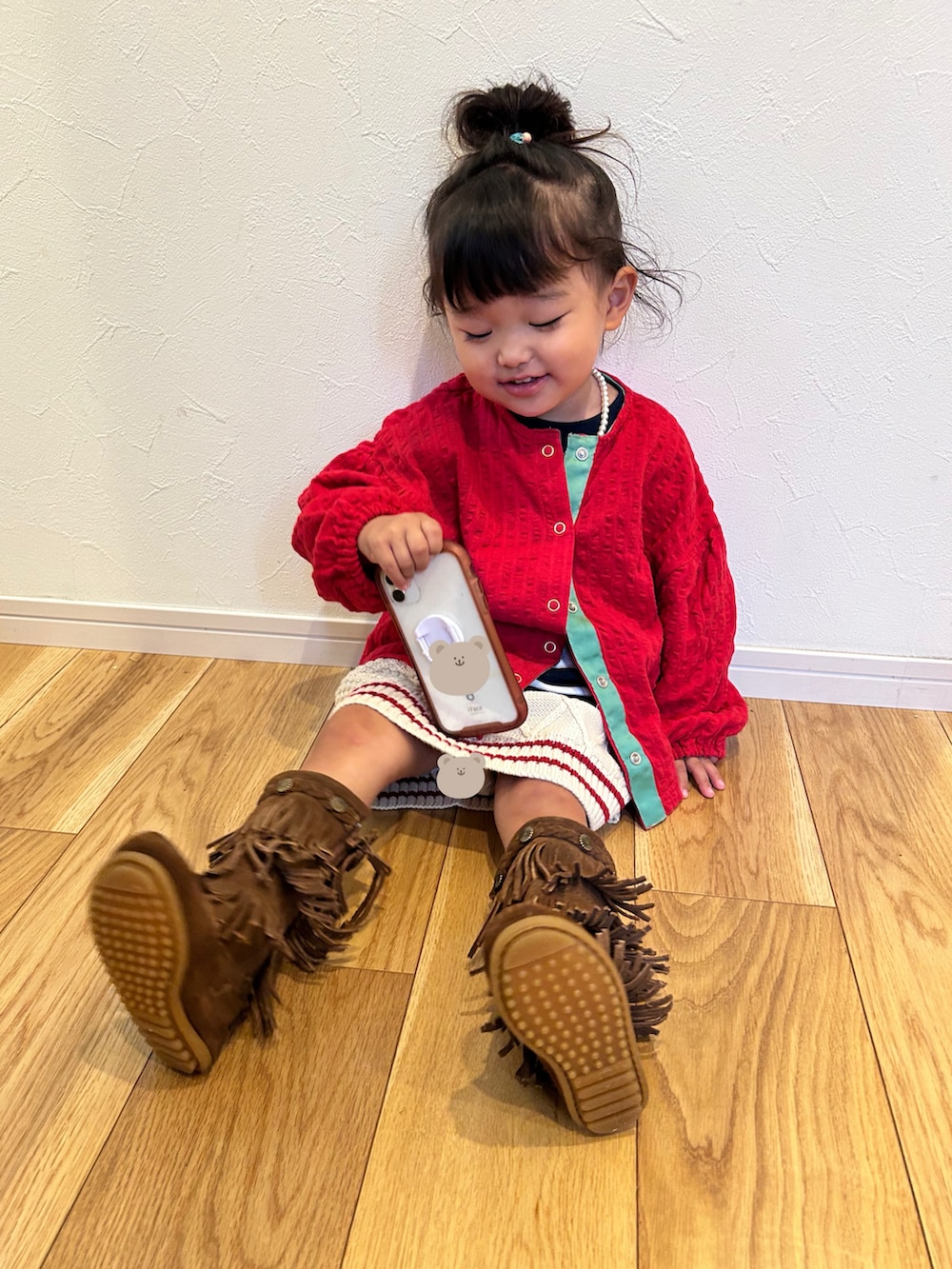 レッド系のカーディガン/ボレロ、ホワイト系のスカート、ブラウン系のブーツを着用したキッズの秋コーディネートの2枚目の写真