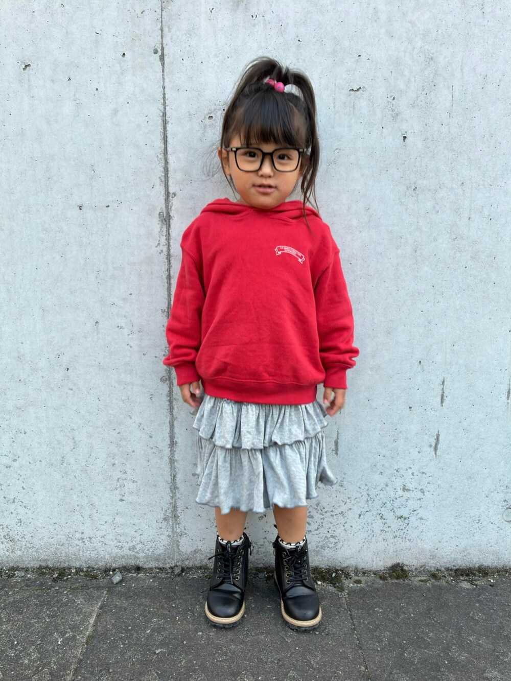 レッド系のパーカー、グレー系のスカート、ブラック系のブーツを着用したキッズの秋コーディネートの2枚目の写真