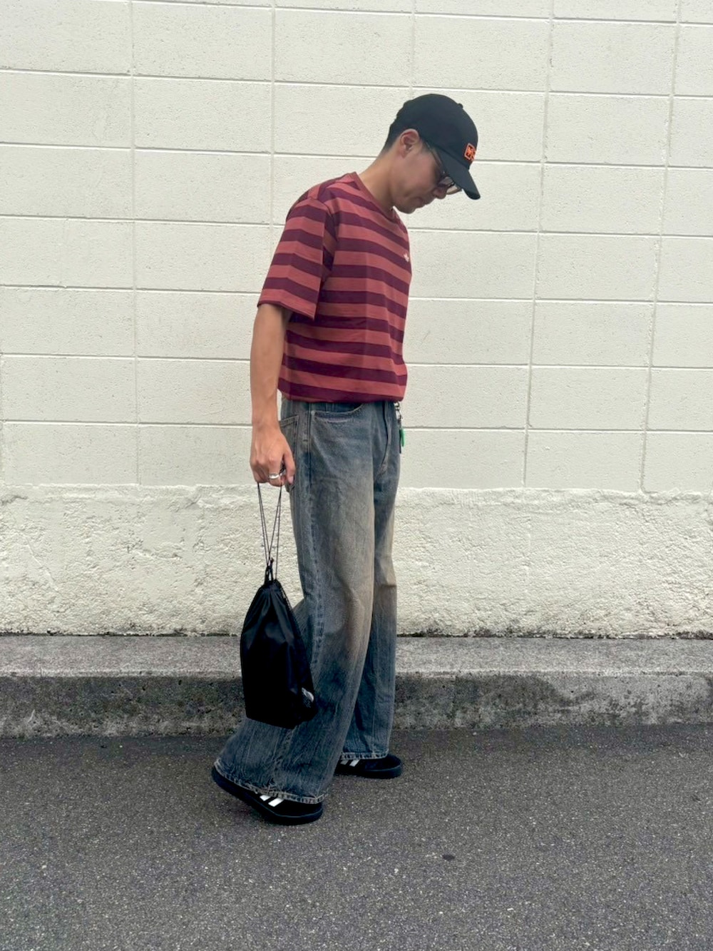 レッド系のTシャツ/カットソー、ブルー系のデニムパンツ、ブラック系のスニーカーを着用したメンズの秋コーディネートの2枚目の写真