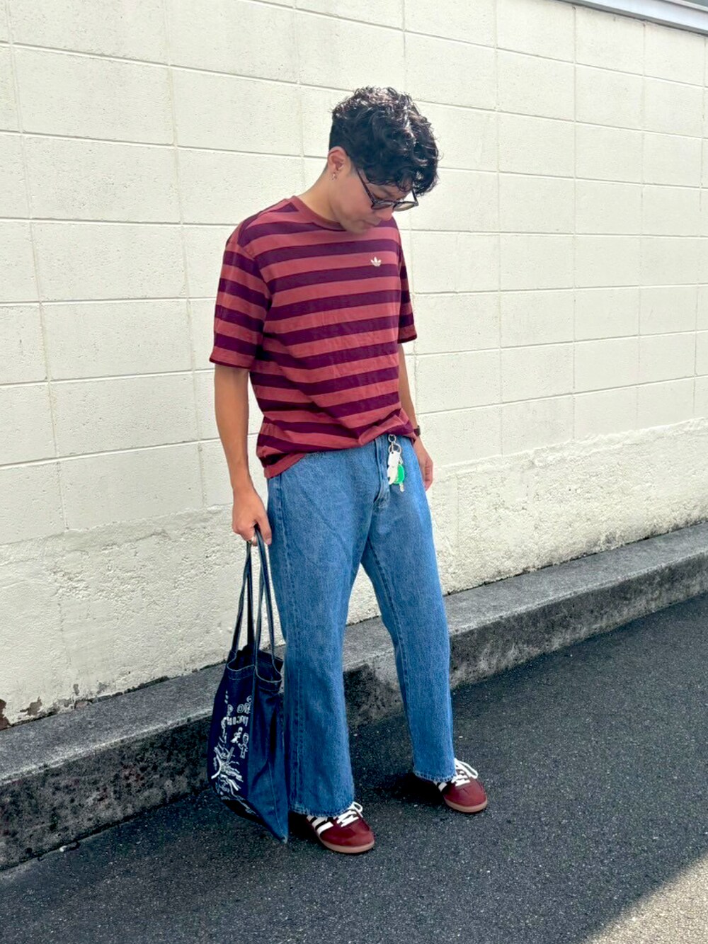 レッド系のTシャツ/カットソー、ブラウン系のスニーカー、ブルー系のデニムパンツを着用したメンズの秋コーディネートの2枚目の写真