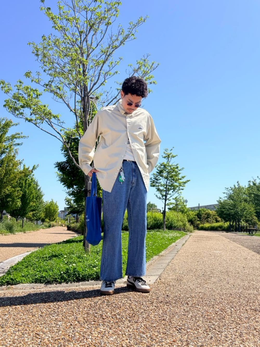 ベージュ系のシャツ/ブラウス、ブルー系のデニムパンツ、ホワイト系のスニーカーを着用したメンズの夏コーディネートの2枚目の写真