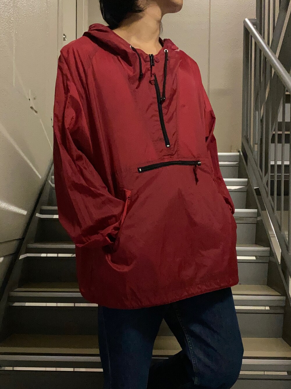 レッド系のナイロンジャケット、ブルー系のデニムパンツ、ブラック系のスニーカーを着用したメンズの夏コーディネートの2枚目の写真