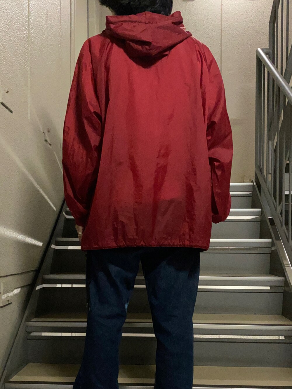 レッド系のナイロンジャケット、ブルー系のデニムパンツ、ブラック系のスニーカーを着用したメンズの夏コーディネートの3枚目の写真