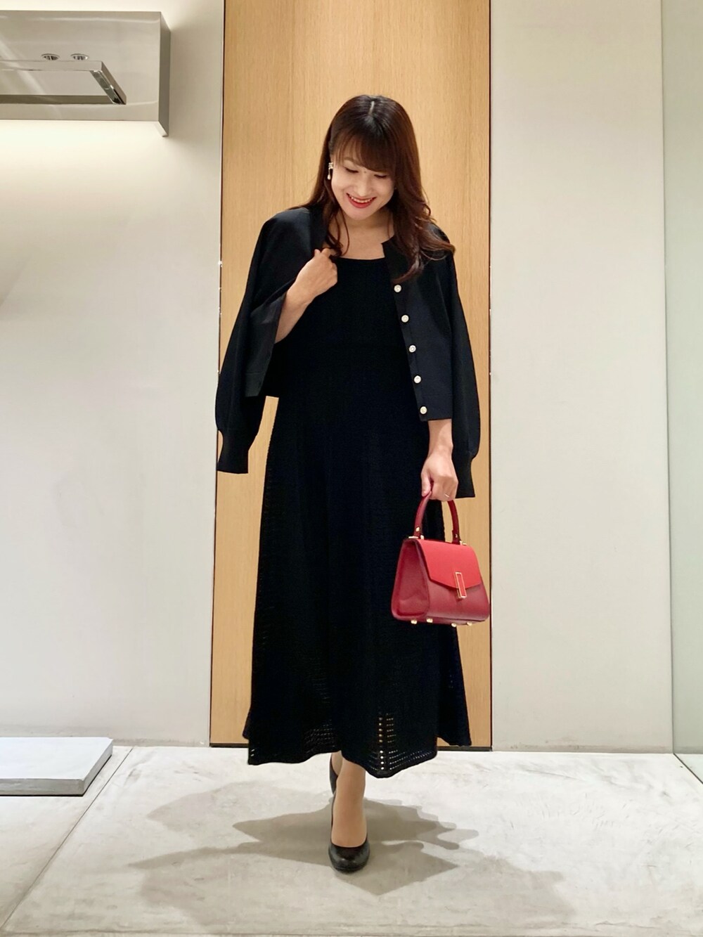 ブラック系のカーディガン/ボレロ、ブラック系のワンピース、レッド系のハンドバッグを着用したレディースの秋コーディネートの2枚目の写真